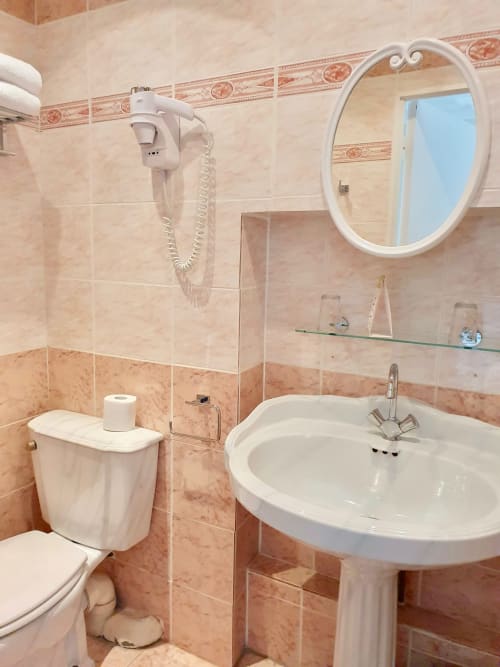 Salle de bain de la chambre de l'hôtel Les Cabines à Houlgate avec lavabo sur piédestal, toilettes, miroir et sèche-cheveux