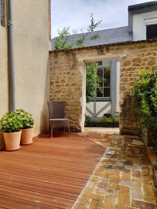 Terrasse de la villa Les Cabines à Houlgate avec terrasse en bois, murs en pierre, plantes en pot et vue sur le jardin