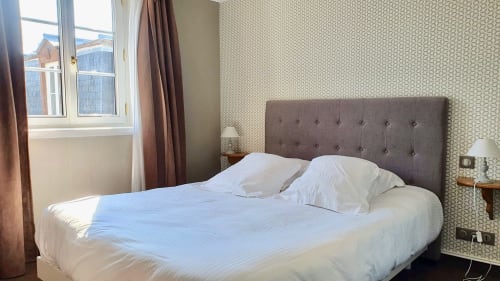 Chambre moderne de l'hôtel Les Cabines avec lit queen-size, tête de lit capitonnée grise et papier peint à motifs à Houlgate