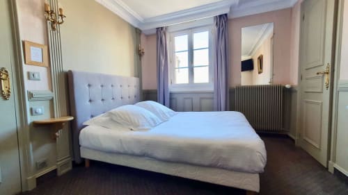 Chambre spacieuse de l'hôtel Les Cabines à Houlgate avec lit queen-size, tête de lit grise, rideaux violets et radiateur.