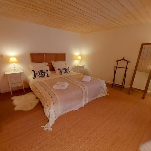 Chambre Perle du Mas De Rigoulac avec plafond en bois, tête de lit en rotin et sol en terre cuite à Argences-en-Aubrac