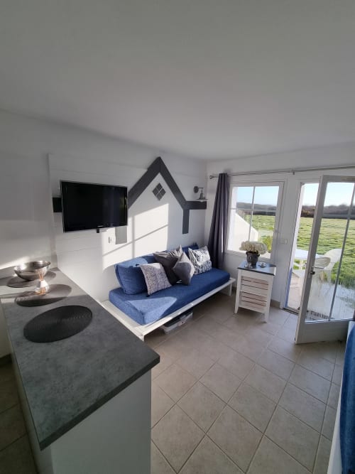 Studio moderne à Loc'Maria, Belle Île en Mer, avec canapé bleu, kitchenette, TV et vue sur mer par les portes vitrées