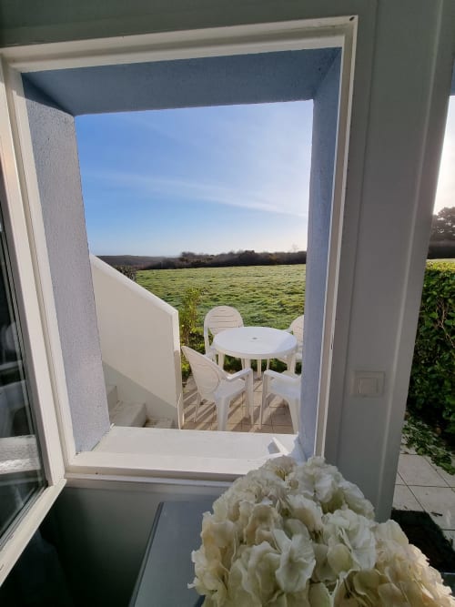 Porte-fenêtre blanche donnant sur une terrasse aménagée avec vue sur les champs verdoyants de l'appartement Loc'Maria, Belle Île-en-Mer