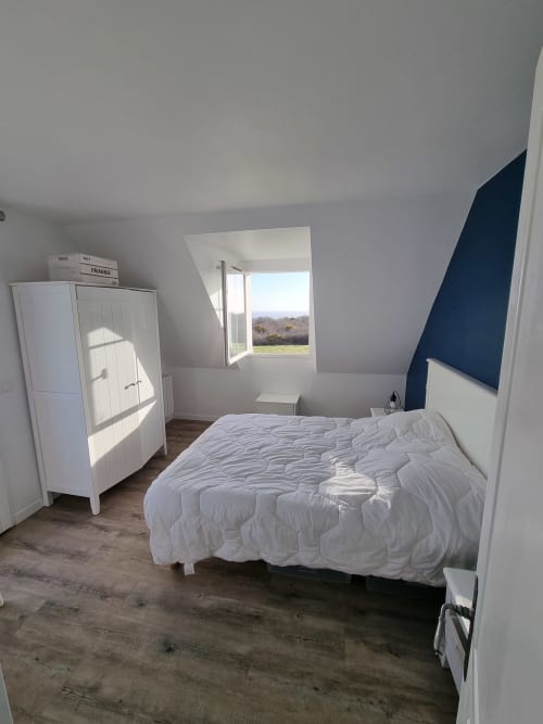 Chambre lumineuse sous les toits à Loc'Maria Belle Île avec lit blanc, armoire, fenêtre sur la campagne, tête de lit bleu foncé