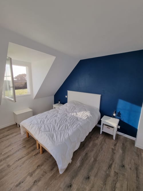 Chambre moderne avec mur d'accent bleu marine, lit blanc, parquet et vue sur Belle-île-en-Mer depuis l'appartement de Locmaria