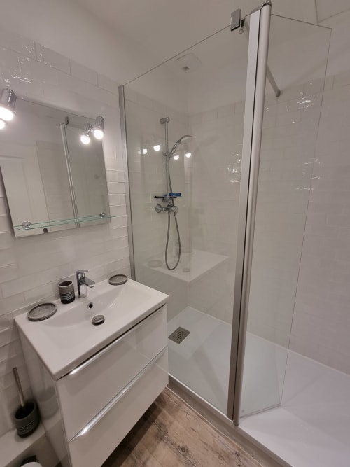 Salle de bain moderne avec lavabo blanc, douche à l'italienne et parquet à l'appartement de vacances Locmaria
