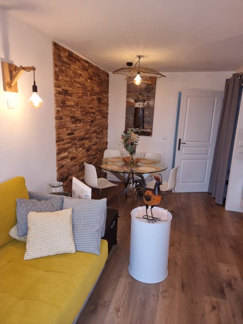Séjour moderne avec canapé jaune, mur de briques, table à manger et vue sur mer à Locmaria Belle Île-en-Mer