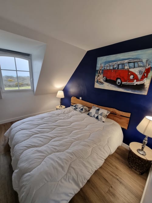 Chambre moderne avec mur d'accent bleu marine, lit en bois, literie blanche, tableau de fourgonnette rouge vintage et vue sur la mer