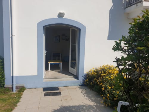 Entrée de l'appartement Résidence 91 à Loc'Maria, Belle Île-en-Mer avec porte cintrée encadrée de bleu et plantes jaunes fleuries
