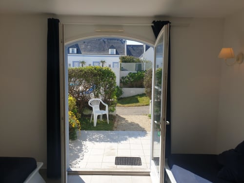 Portes-fenêtres ouvertes donnant sur le jardin intérieur de l'appartement de vacances Locmaria Belle Île en Mer, avec chaise blanche et aménagement paysager