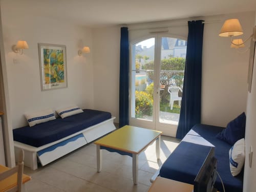 Lumineux séjour avec mobilier bleu marine, table jaune et baies vitrées donnant sur la piscine à Locations Loc'Maria