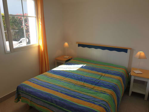 Chambre lumineuse aux Locations Loc'Maria, Belle Île-en-Mer, avec literie rayée, mobilier en bois et vue sur le jardin