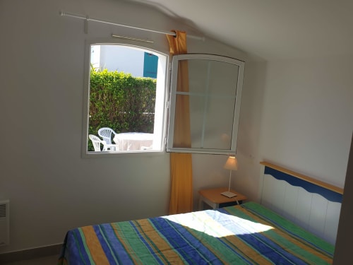 Chambre lumineuse de l'appartement de Locmaria avec literie rayée, fenêtre ouverte sur le jardin, mobilier en bois et lampe de table