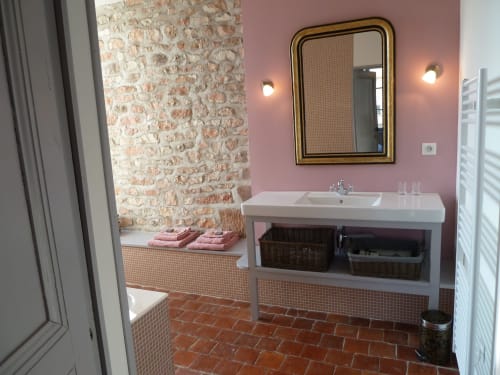 Salle de bain moderne au Château De Clusors : murs rose pâle, accent de brique, vasque blanche et paniers de rangement tressés