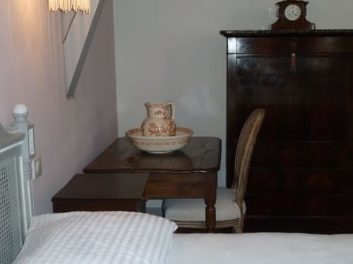 Dormitorio vintage en el Château De Clusors con muebles de madera antigua, jarra y palangana de cerámica, y decoración tradicional