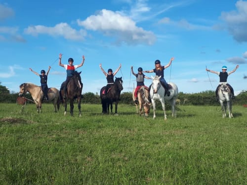 Jeunes cavaliers les bras levés montant à cheval dans un champ herbeux à La Maison De Fleurat, Domeyrot