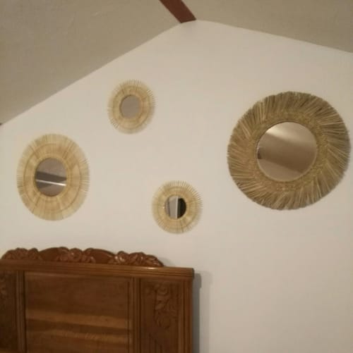 Détail de la décoration murale au-dessus du lit dans la Chambre Familiale Soleil. Composition de quatre miroirs ronds suspendus sur un mur blanc. Trois petits miroirs avec cadres en fines tiges de rotin et un grand miroir avec cadre en raphia tressé. Tête de lit en bois sculpté visible en bas de l'image.