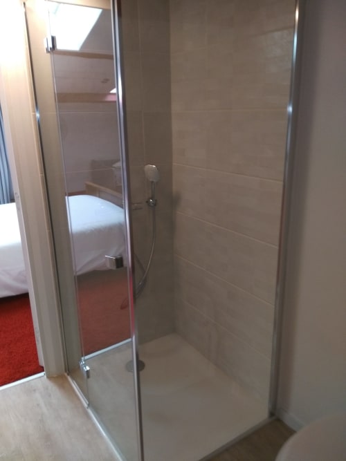 Cabine de douche moderne à porte en verre transparente de la chambre Soleil, avec carrelage texturé beige et vue sur la chambre adjacente.
