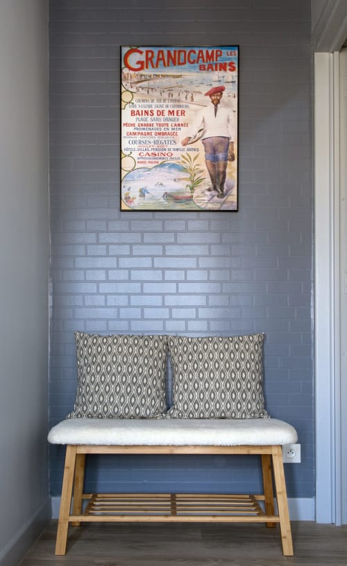 Vintage Grandcamp-les-Bains beach poster above wooden bench with patterned cushions at Au Gite d'Isigny, Normandy
