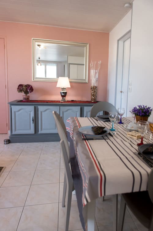 Dining room at Au Gite d'Isigny B&B with pink walls, striped table runner, and blue sideboard in Isigny-sur-Mer