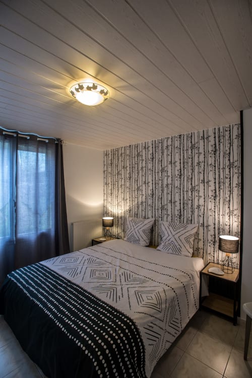 Cozy cottage bedroom at Au Gite d'Isigny with patterned wallpaper, geometric bedding, and ceiling light in Isigny-sur-Mer