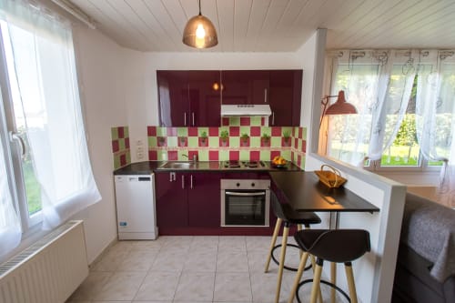 Modern cottage kitchen with burgundy cabinets, red and green tile backsplash, black countertop bar seating, and garden views