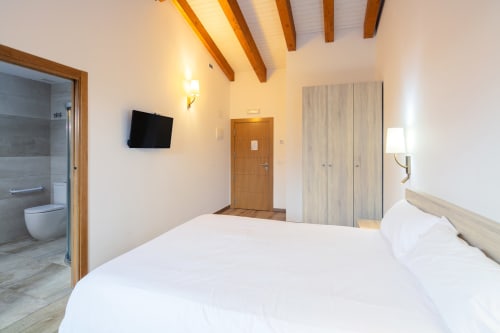 Quarto moderno em O Trancallo com cama branca, TV, vigas de madeira, banheiro privativo e vistas para as montanhas de Ourense