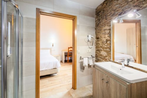 Banheiro moderno do O Trancallo B&B em Ourense com parede de pedra, bancada de madeira e porta aberta para o quarto