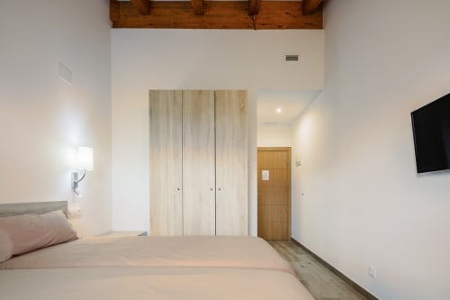 Quarto de casal moderno no O Trancallo BnB em Ourense com guarda-roupas em madeira clara, cama com luminária de cabeceira, TV na parede