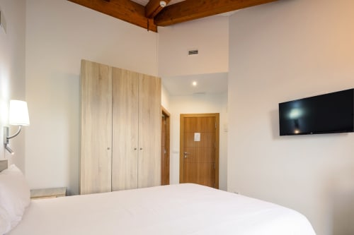 Quarto casal moderno em O Trancallo com guarda-roupa em madeira clara, TV de parede e vigas de madeira aparente em Ourense