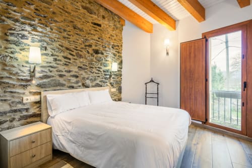 Quarto de casal moderno no O Trancallo BnB em Ourense com parede de pedra, vigas de madeira, vistas para a montanha e porta de madeira para a varanda