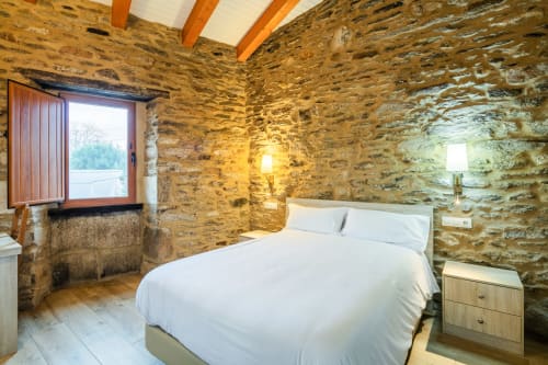 Quarto rústico de pedra em O Trancallo em Ourense com cama queen, vigas de madeira e vista para as montanhas