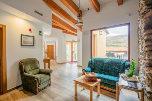 Spacieux salon d'O Trancallo à Mourisca avec poutres apparentes, fauteuil vert, canapé bleu-vert et vue sur la campagne