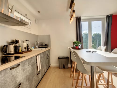 Cuisine-salle à manger moderne à la Résidence L'Hermitière avec cuisine équipée, table blanche et baies vitrées donnant sur jardin