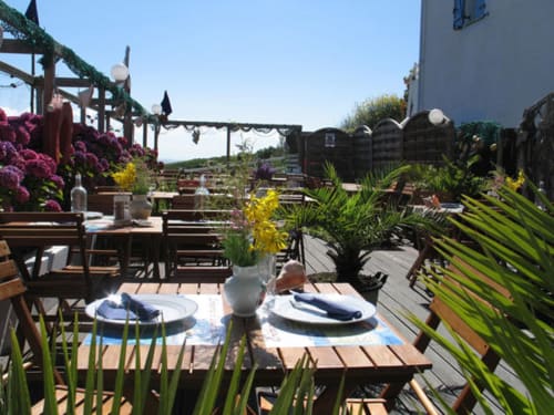 Élégante terrasse de dining en plein air avec fleurs violettes, plantes en pots et mobilier bois à Loc'Maria, Belle Île en