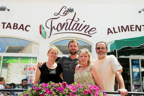 Quatre personnes souriantes devant la boutique La Fontaine à Locmaria, Belle-Île-en-Mer, avec des fleurs roses
