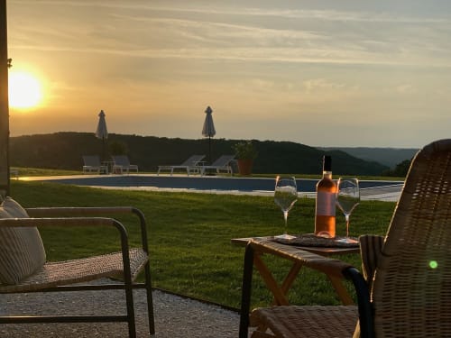 Sunset view at Domaine De Cazal with wine glasses, infinity pool, and lounge chairs overlooking Saint-Cyprien countryside