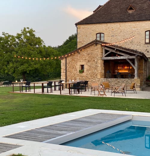 Domaine De Cazal luxury pool and patio at dusk with stone manor house, outdoor fireplace and dining area