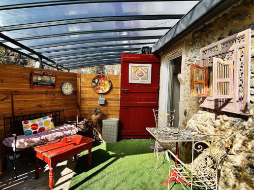 Terrasse privée et abritée du studio : salon de jardin, murs en pierres et verrière pour profiter de l'extérieur en toute saison.