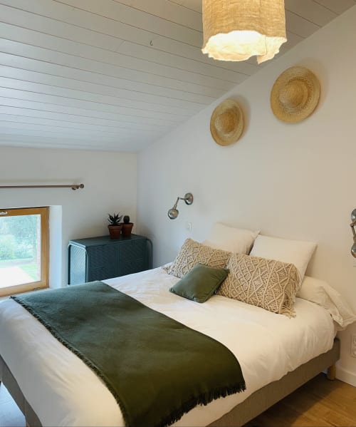 Chambre lumineuse à la Maison Monsieur Léger avec draps blancs, coussins décorés et paniers tressés muraux à Montaut, France