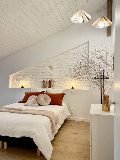Chambre moderne à la Maison Monsieur Léger avec draps blancs, coussins rouille, plafond mansardé et luminaires suspendus à Montaut