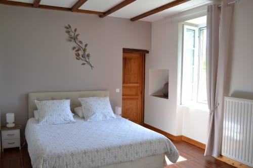 Bright bedroom at Logis De La Bénétière with queen bed, wooden beams, and garden view door in Treize-Vents