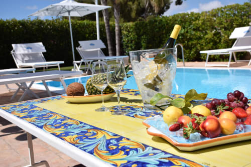 Tavolo in piscina a Villa Blanche Holidays a Marsala con vino, frutta fresca e vista mediterranea