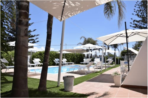 Zwembadgebied van Villa Blanche Holidays in Marsala met ligbedden, parasols, palmbomen en verzorgd gazon