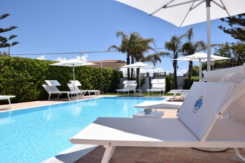 Esclusiva area piscina a Villa Blanche Holidays a Marsala con lettini, ombrelloni e palme sotto cielo blu