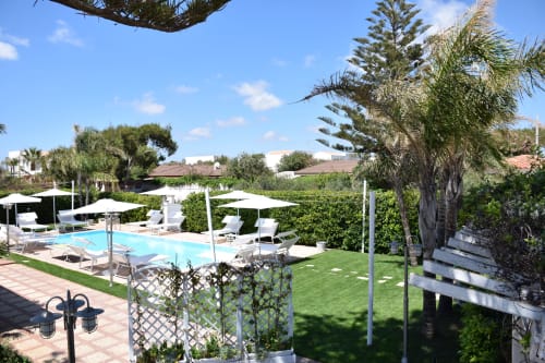 Area piscina di Villa Blanche Holidays a Marsala con lettini, ombrelloni, palme e prato verde
