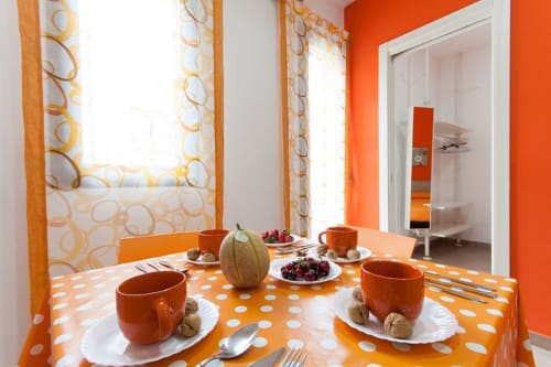 Vivace zona pranzo arancione nell'Apartment Orange di Casa Vacanze Del Golfo con tavolo a pois, frutta fresca e vista sulla città
