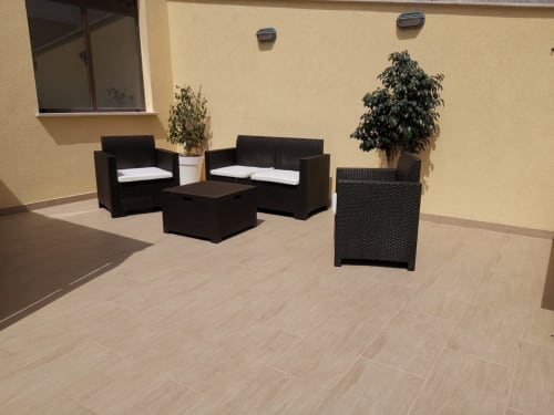 Sunny terrace at Casa Vacanze Del Golfo with black wicker seating, potted plants, and cream-colored tiled floor overlooking