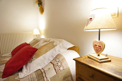 Cozy bedroom at L'étape Du Fanfoué in Chamrousse with red pillow, wooden nightstand, and decorative heart lamp