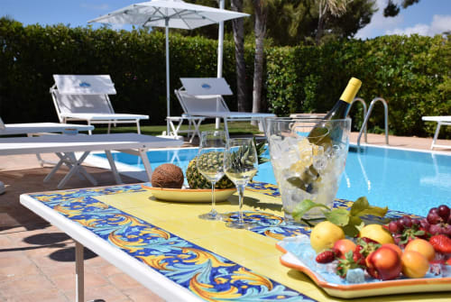 Tavolo a bordo piscina con vino, frutta e cocktail a Villa Blanche Holidays a Marsala, Italia